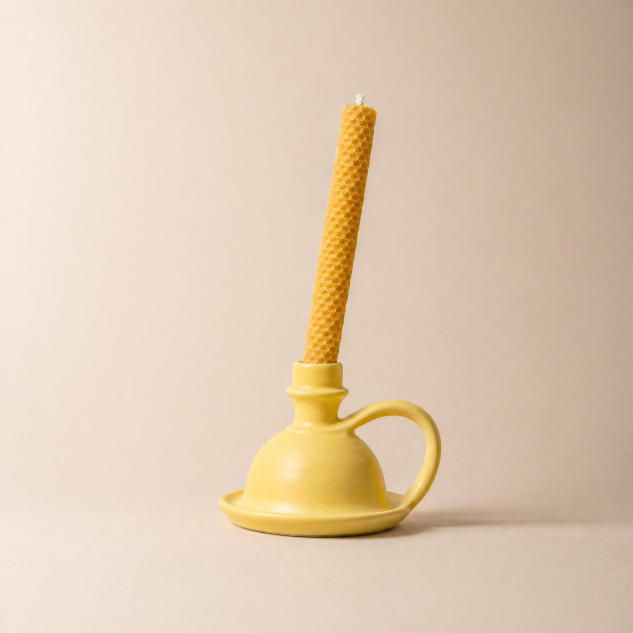 Yellow candle holder with a textured yellow candle on a beige background