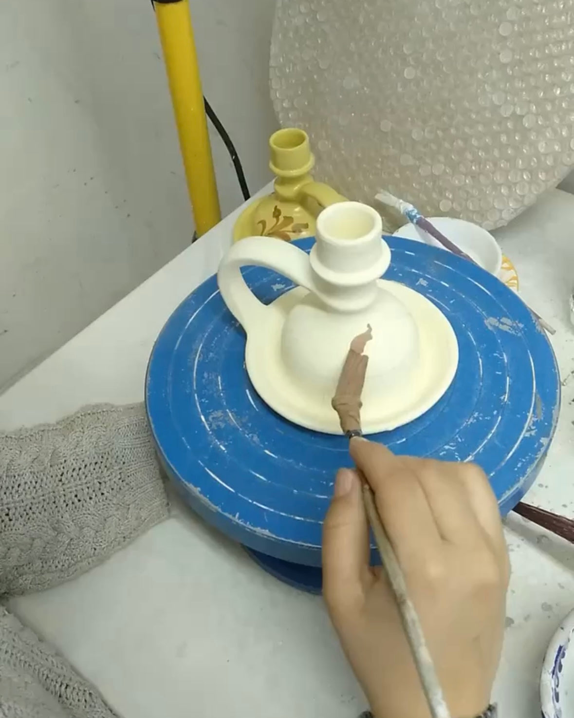 Person working on a ceramic piece on a turntable with tools in the background.
