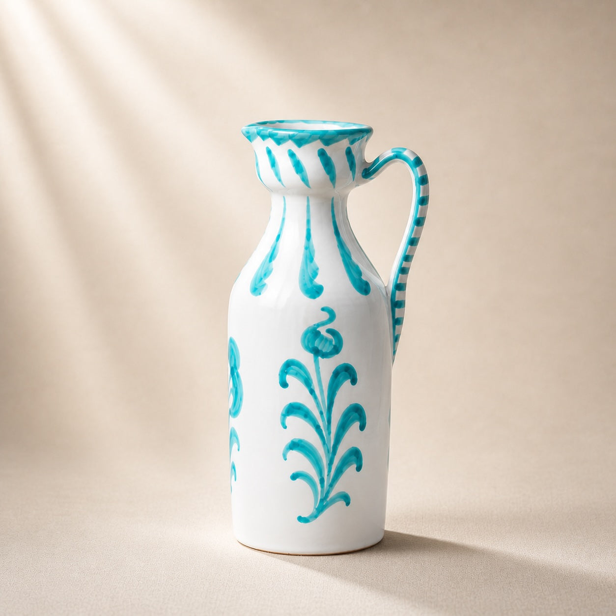 White ceramic pitcher with turquoise floral patterns on a beige background