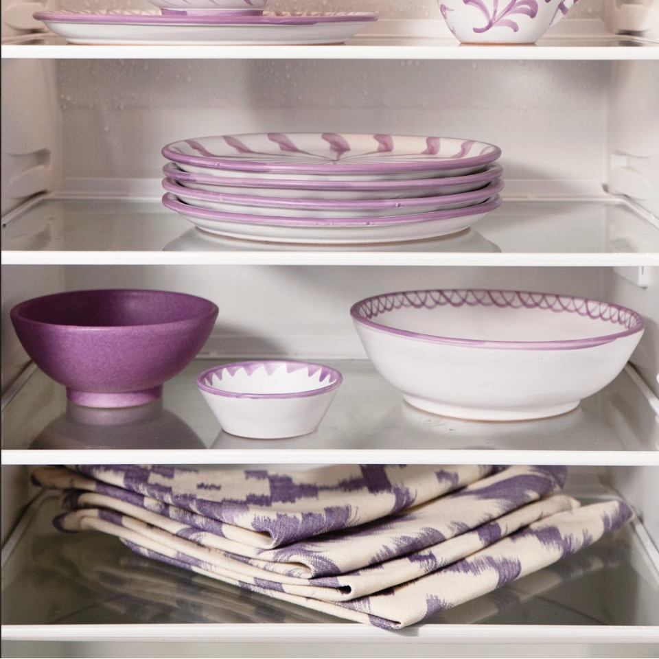 Purple and white ceramic dishes and tableware arranged on a refrigerator shelf.