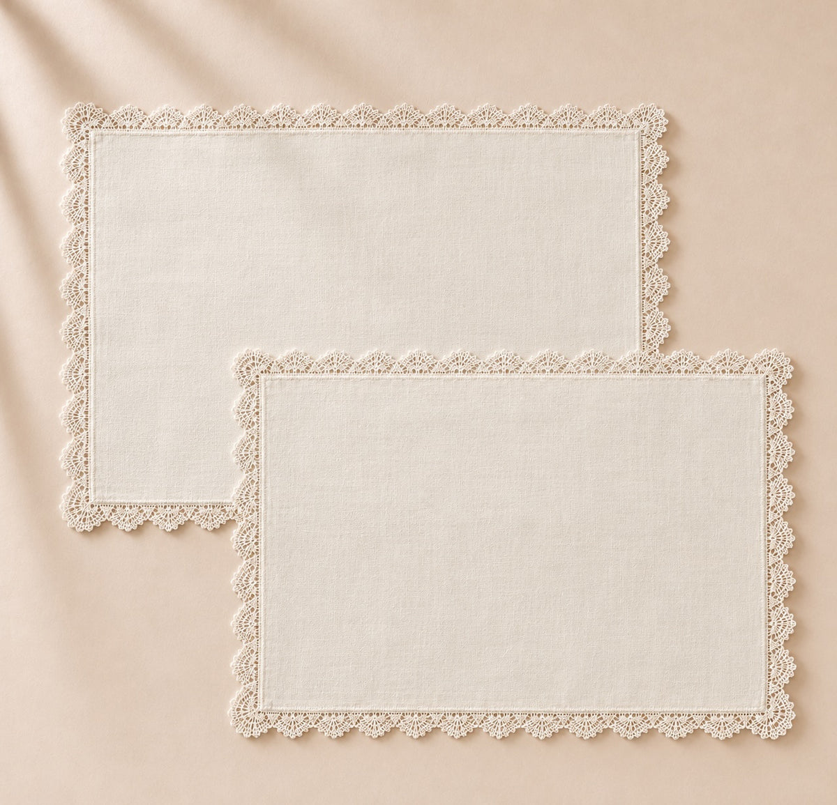 Two rectangular cream linen placemats with delicate floral lace scalloped edges, arranged diagonally on a matching beige background.