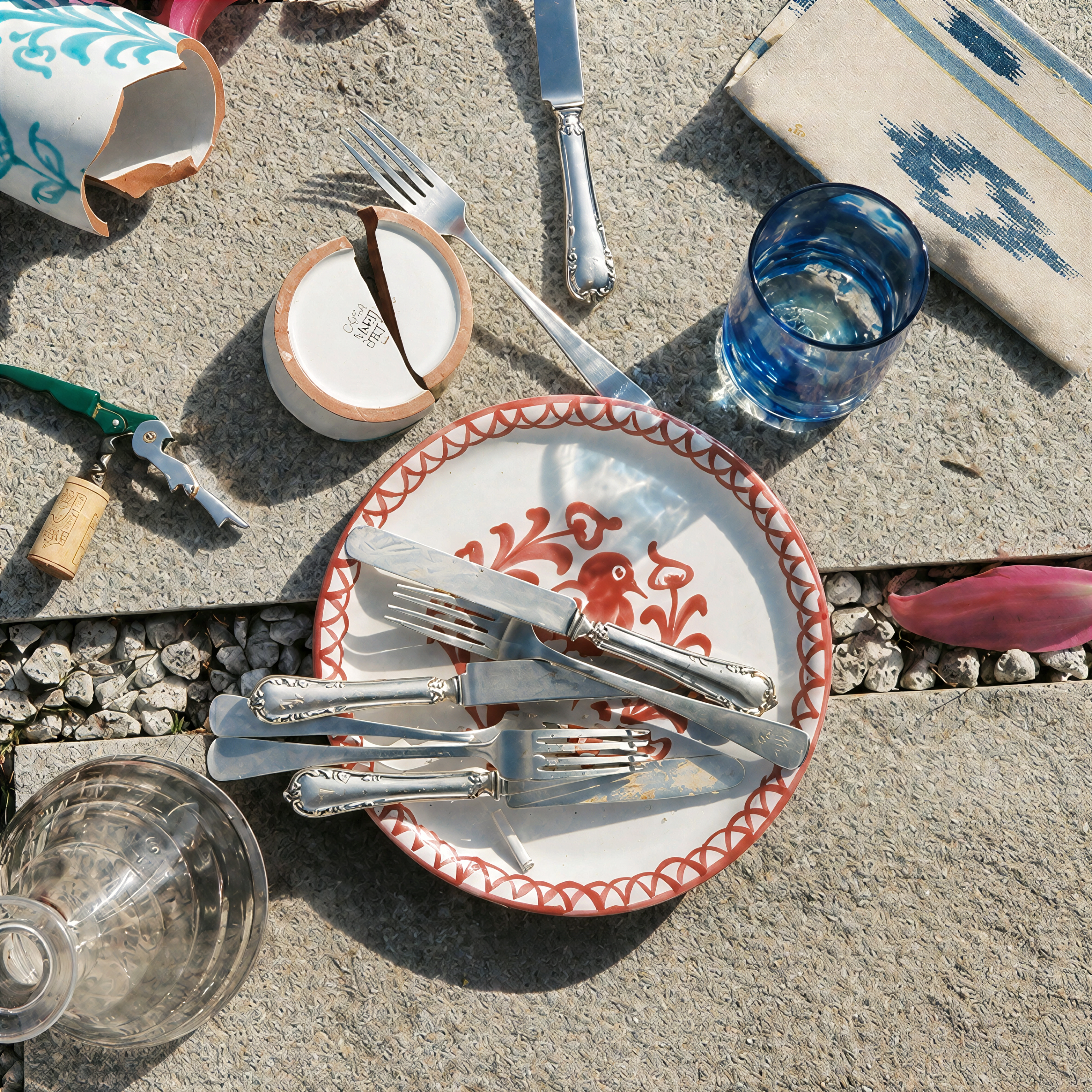 A styled tabletop setting featuring a cream-colored ceramic plate with a blue marbled pattern, layered on a matching plate. The setting includes silver cutlery, a small cream cup, a striped napkin, and a blue-and-white embroidered tablecloth. - lifestyle