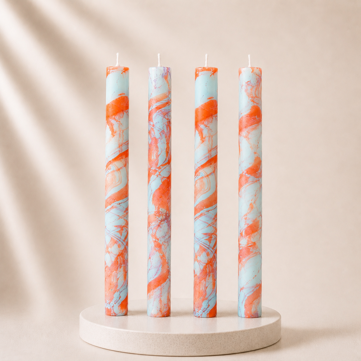 Four marbled candles with orange and blue patterns on a beige background