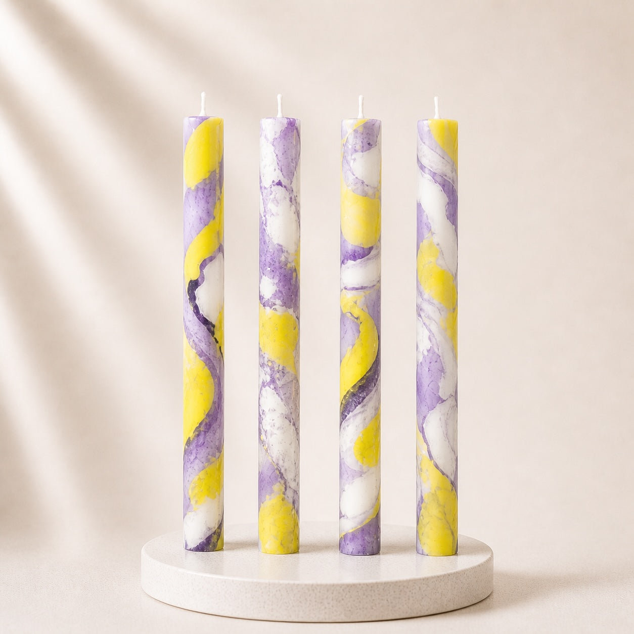 Four marbled candles in purple and yellow on a white stand against a beige background