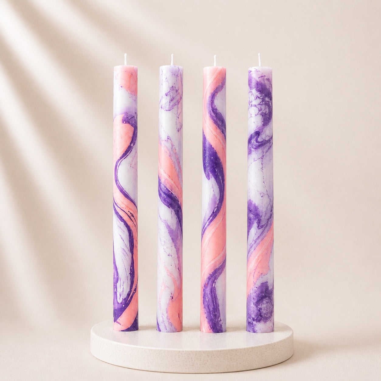 Four marbled candles in pink and purple on a white stand against a beige background