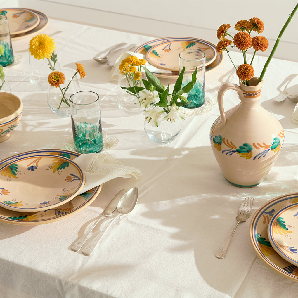 Decorative table setting with floral arrangements, ceramic plates, and a pitcher on a white tablecloth.