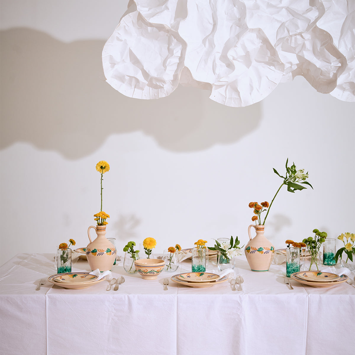 Decorative table setting with ceramic plates, glasses, and vases on a white tablecloth.