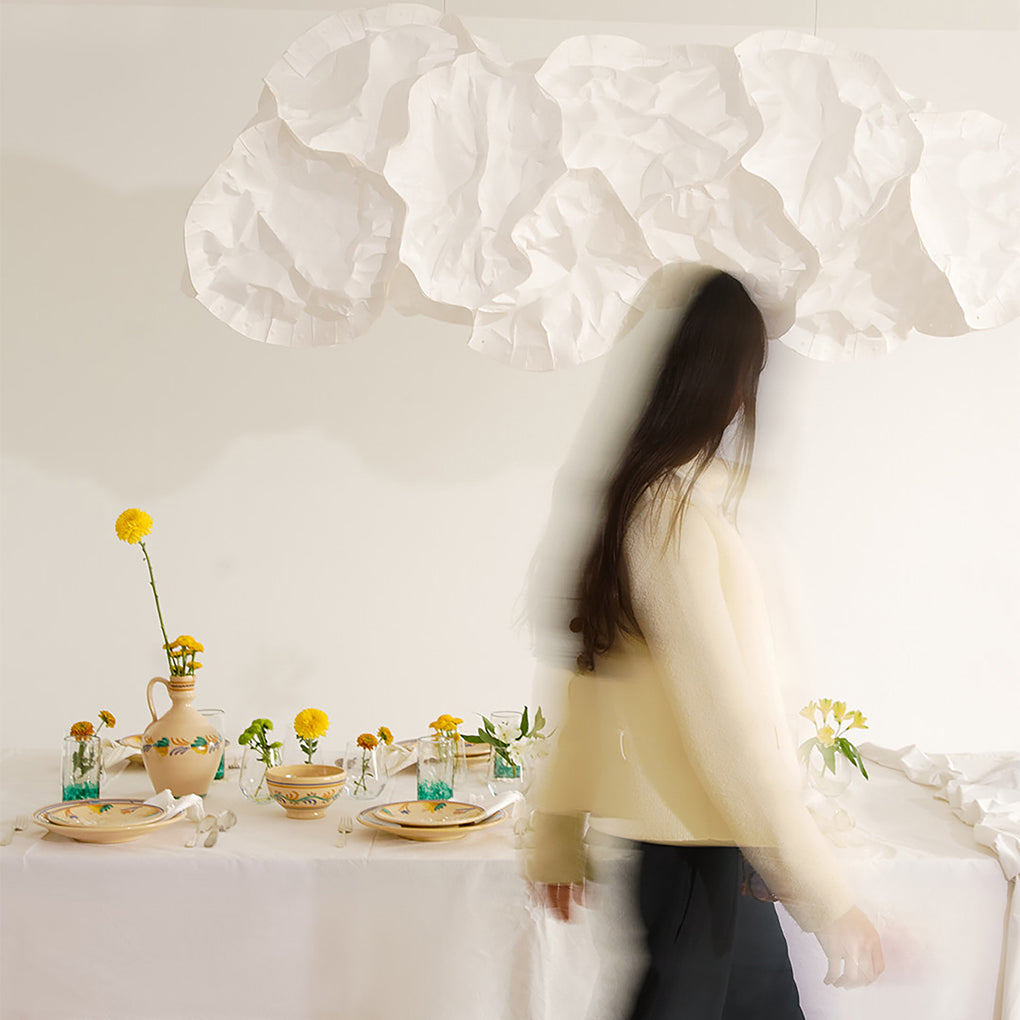 Woman standing in a room with a table set for a meal, featuring flowers and a vase.
