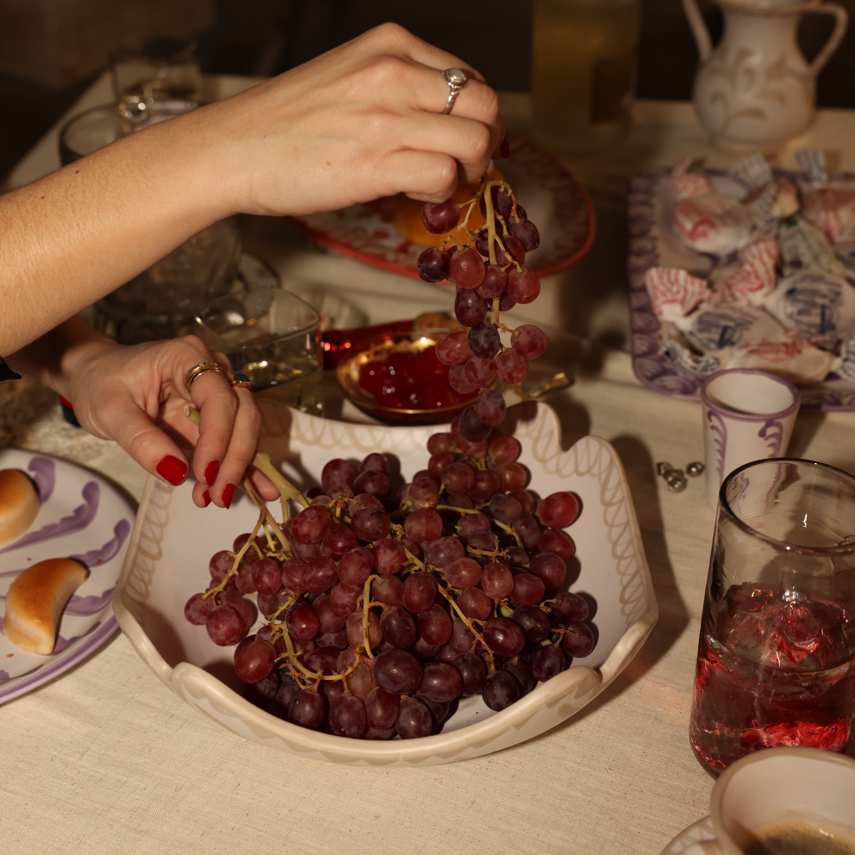 Person arranging grapes on a plate with a table setting in the background