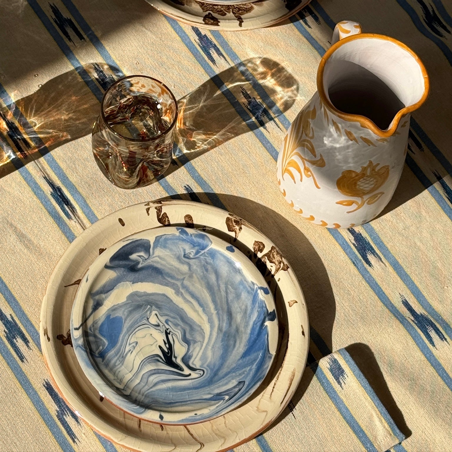 deflated glass, traditional pitcher, brwon marbled dinner plate, blue linen and blue side plate on table - lifestyle