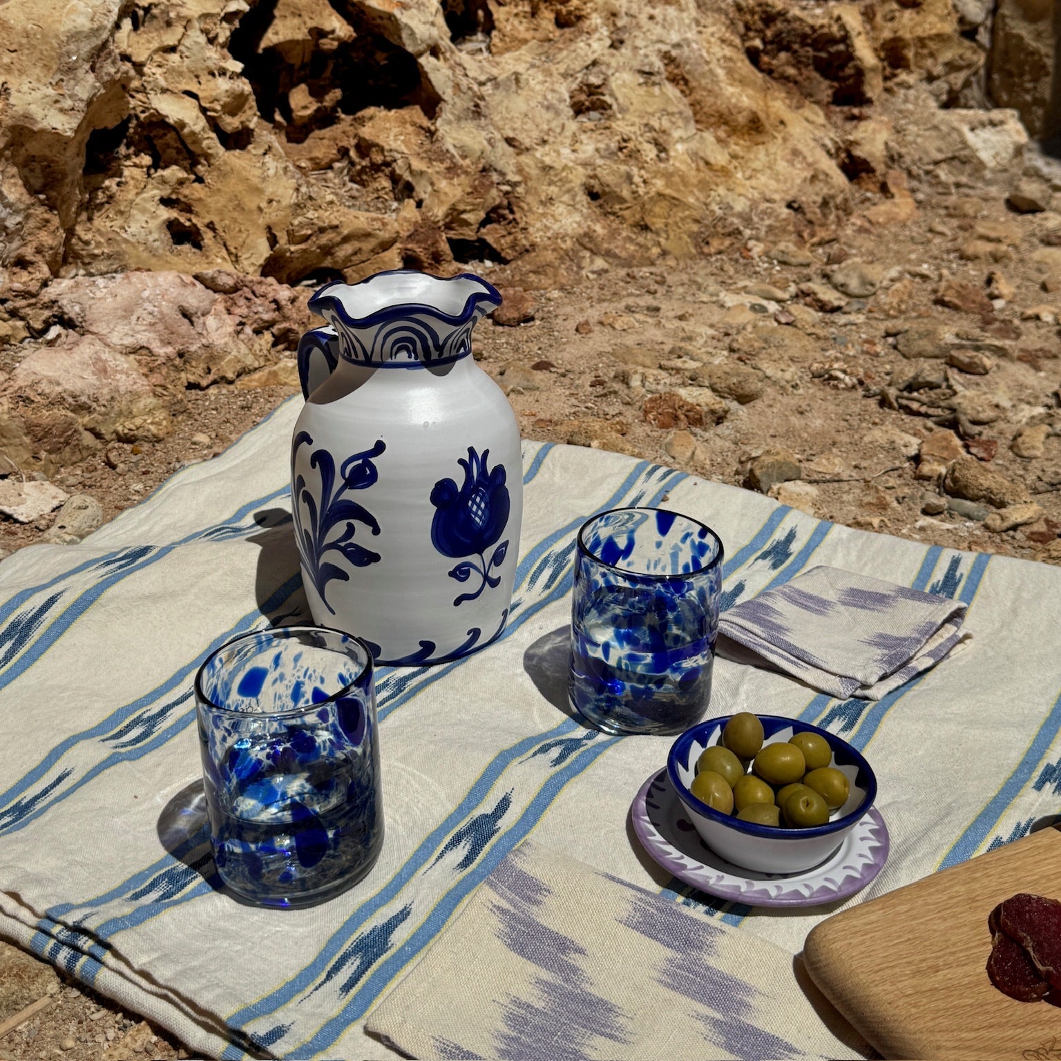Ceramic pitcher and glasses on a tablecloth with a stone wall background - lifestyle
