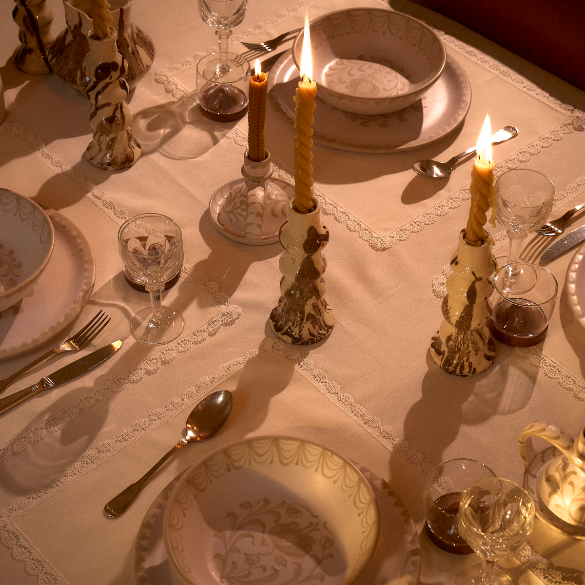 A place setting on a table featuring a cream-colored ceramic bowl with a gold damask pattern, resting on a matching scalloped plate. The setting includes gold-toned cutlery, a glass, and other dining accessories under warm, ambient lighting. - lifestyle