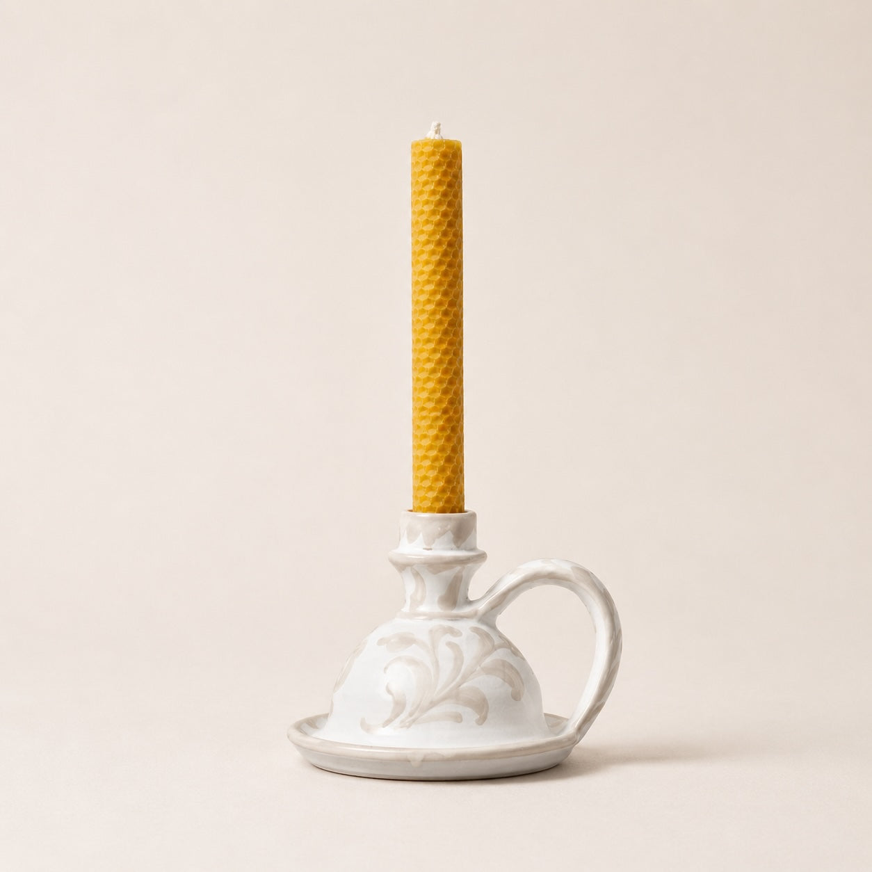 White ceramic candle holder with a yellow candle on a beige background
