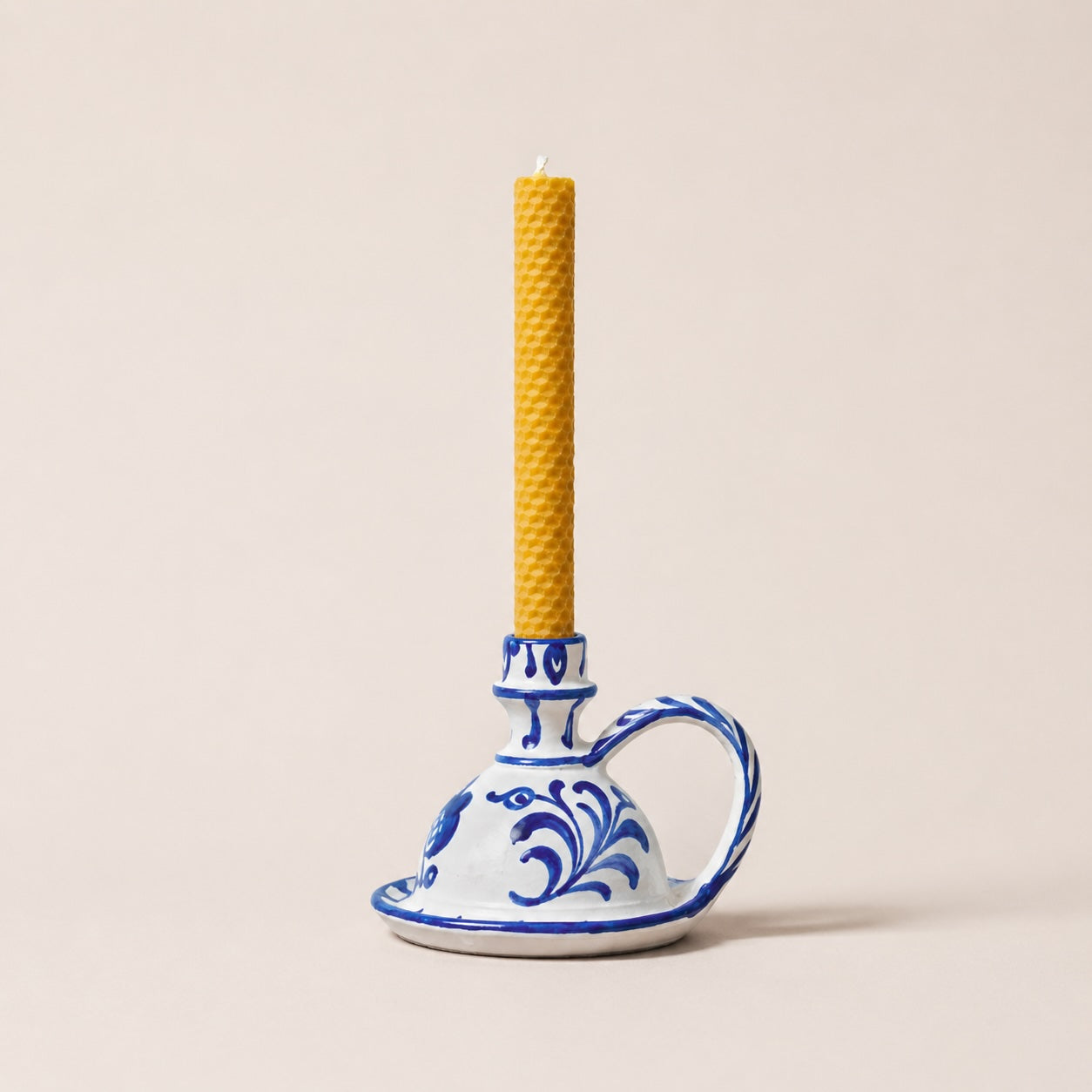 Candle holder with blue floral design holding a beeswax candle on a beige background