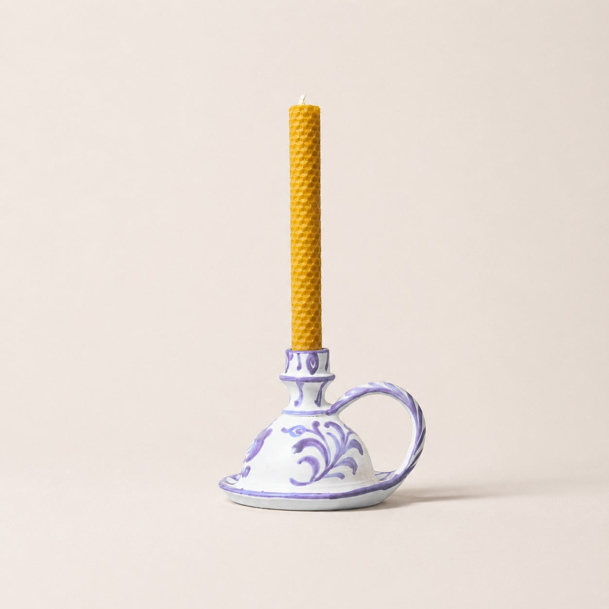 Yellow candle in a decorative ceramic holder on a beige background