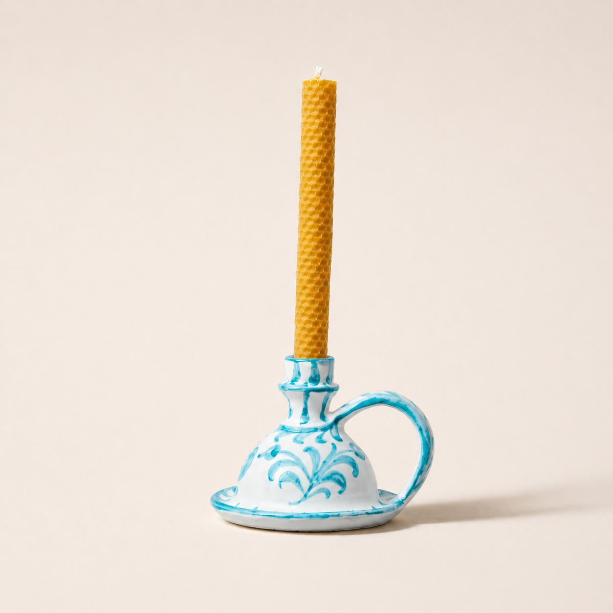Ceramic candle holder with a blue design holding a tall, textured yellow candle on a beige background