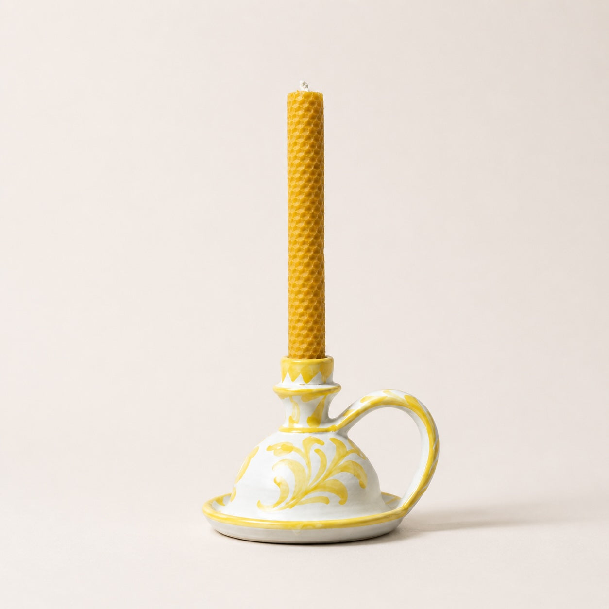 Yellow textured candle in a decorative ceramic holder on a light beige background