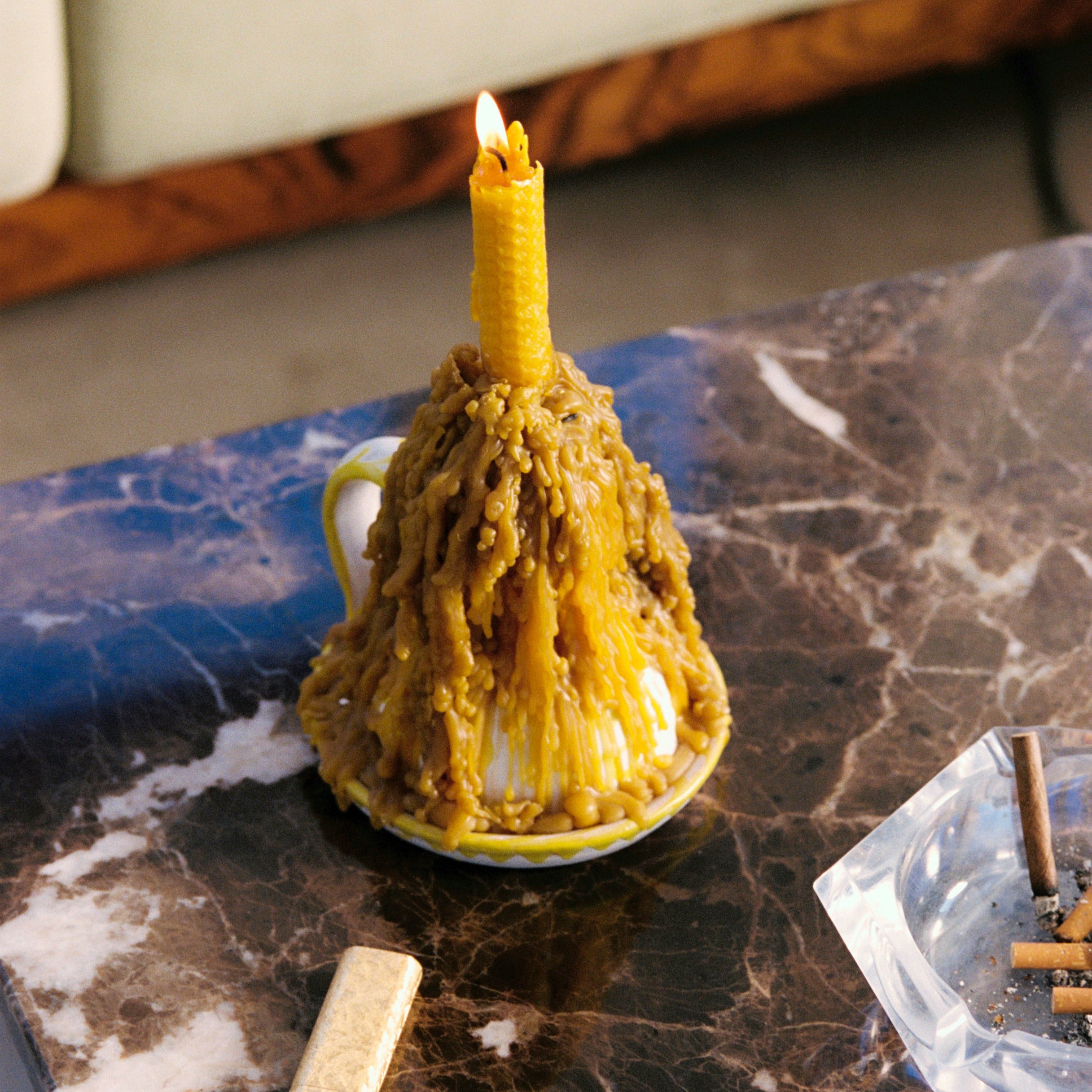 Burnt candle in a white cup on a marble surface with matches and an ashtray.