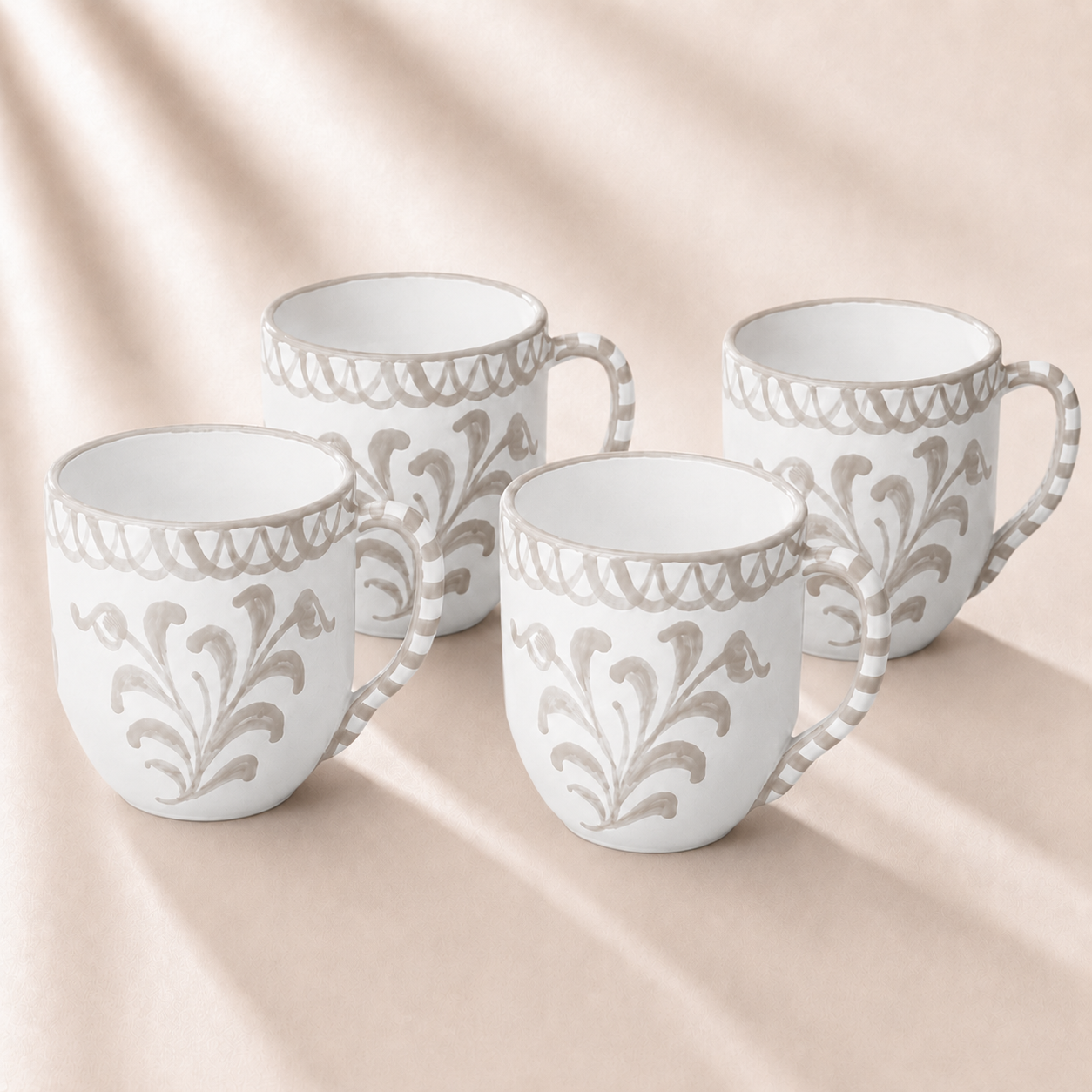 Set of four white mugs with decorative patterns on a beige background