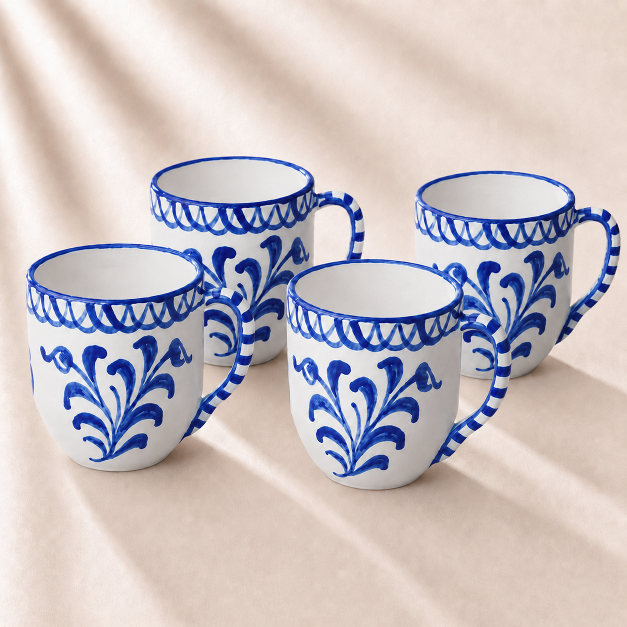 Four white mugs with blue floral patterns on a beige fabric background
