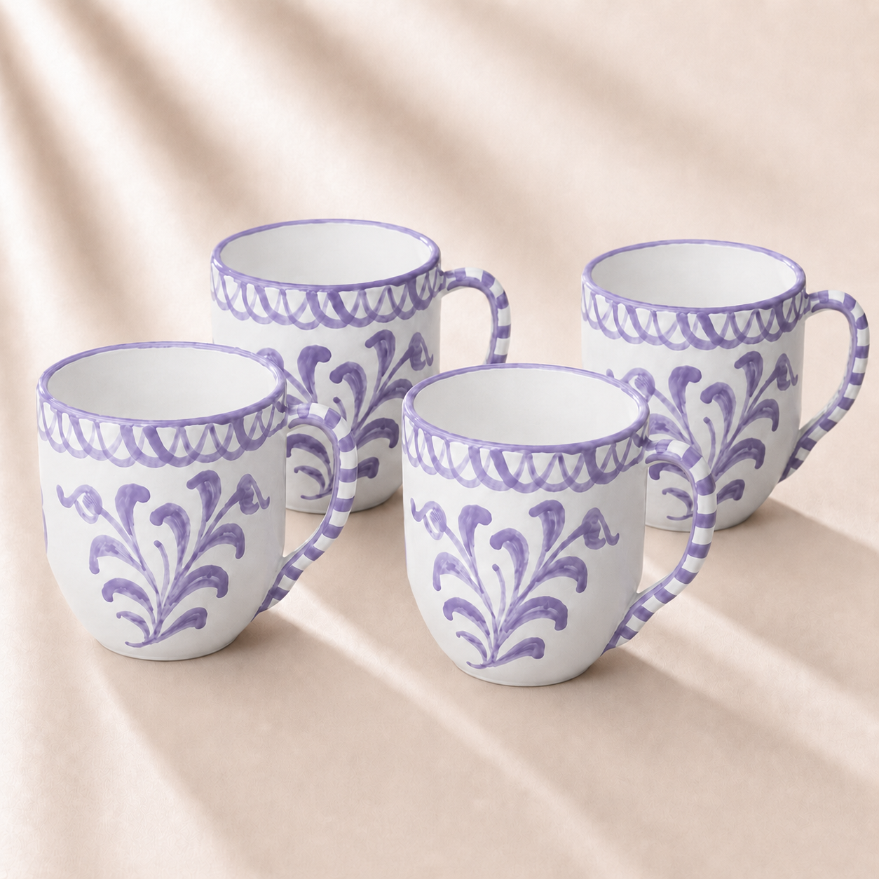 Four ceramic mugs with purple floral patterns on a beige fabric background