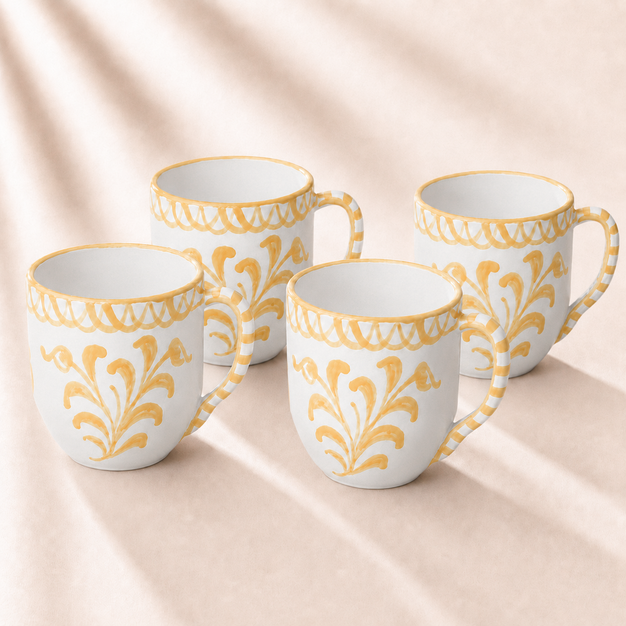 Four white mugs with yellow floral patterns on a beige fabric background