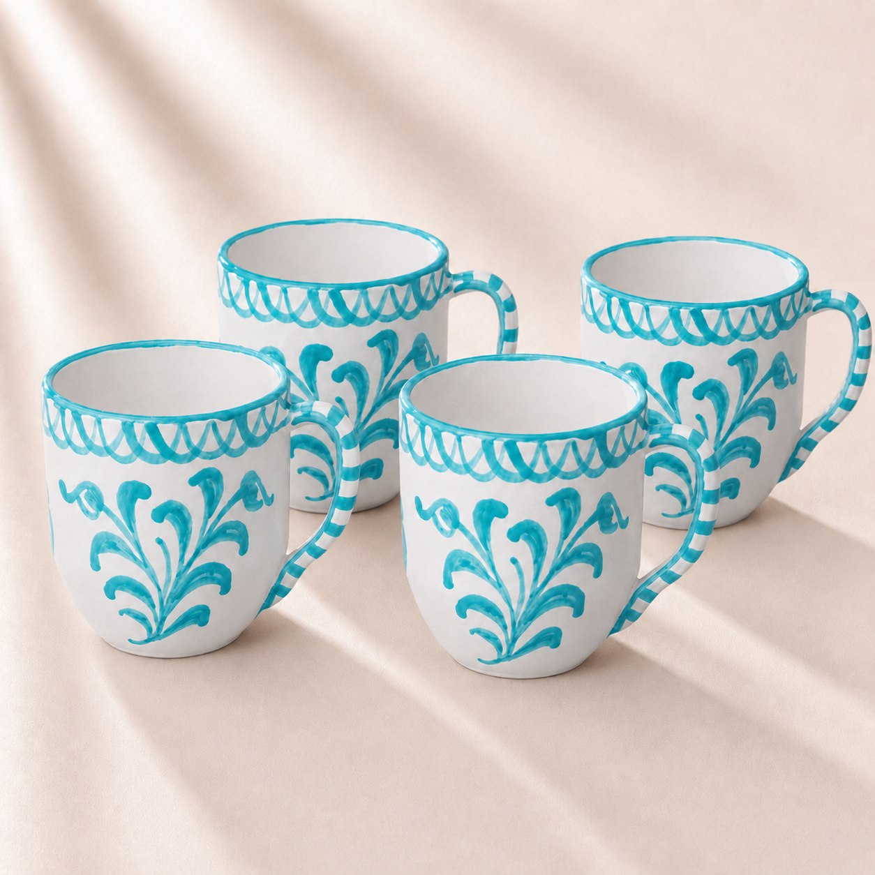 Four ceramic mugs with turquoise decorative patterns on a beige background