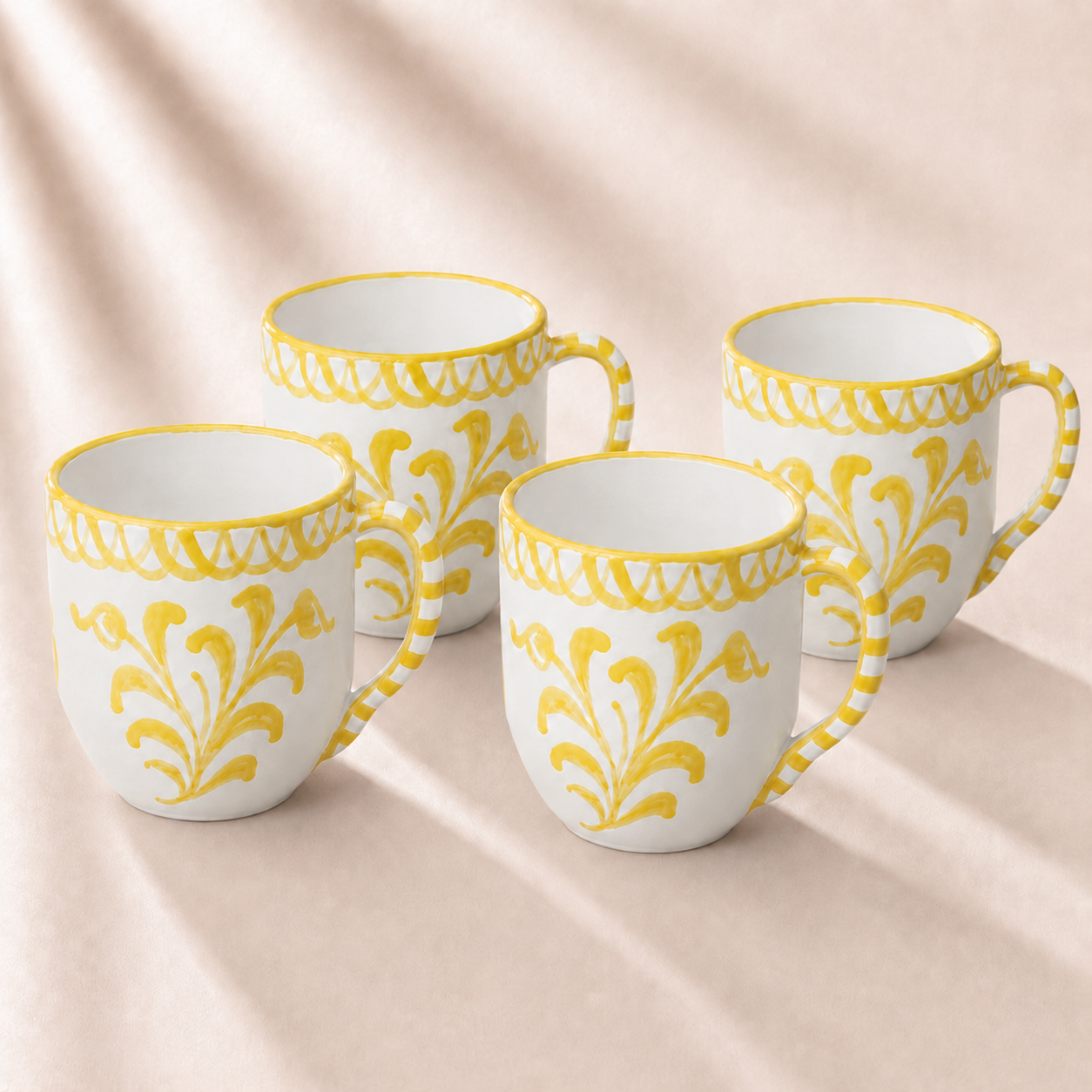 Four white mugs with yellow decorative patterns on a beige fabric background