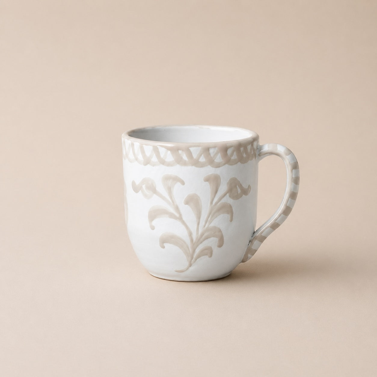 White ceramic mug with decorative floral pattern on a beige background