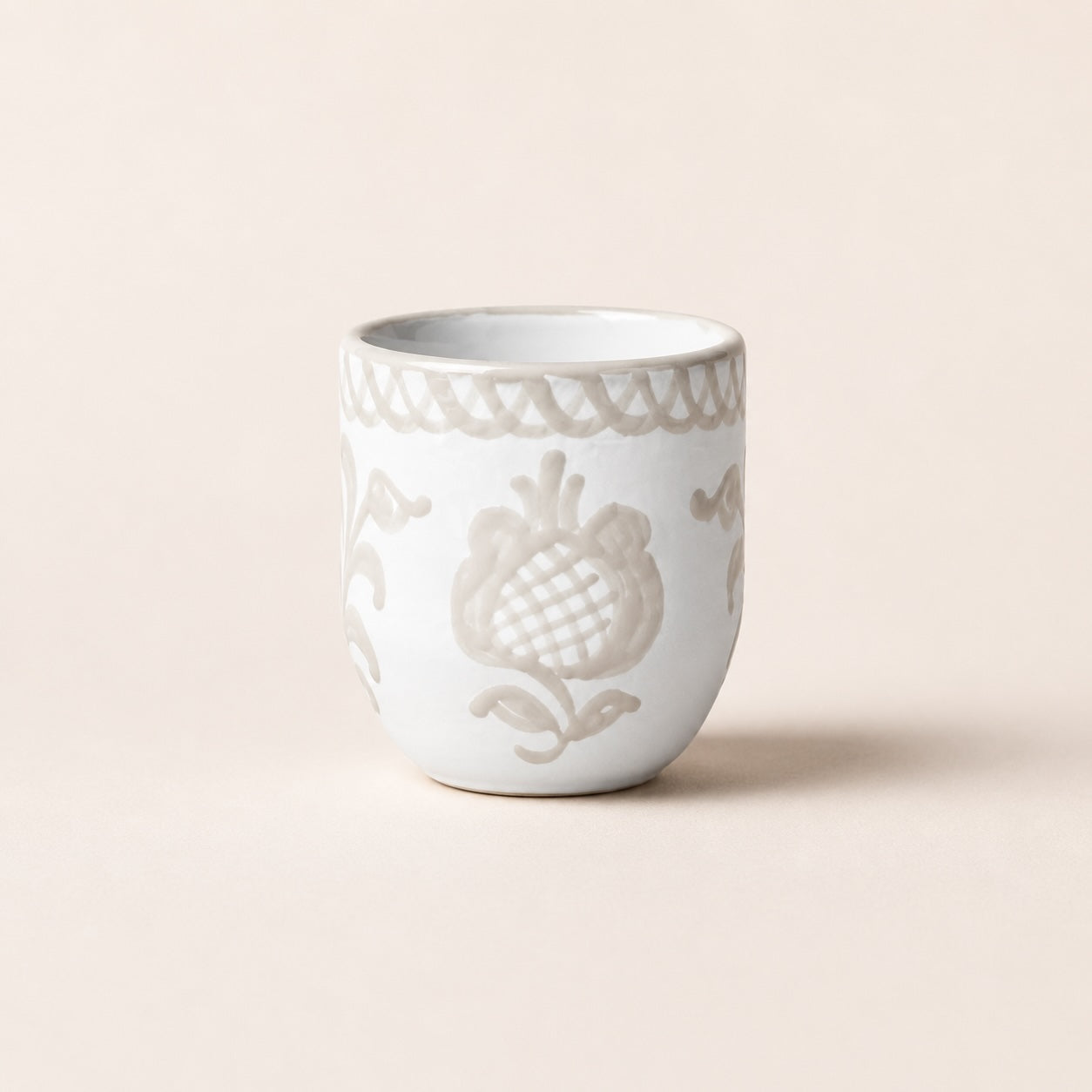 White ceramic cup with decorative patterns on a beige background