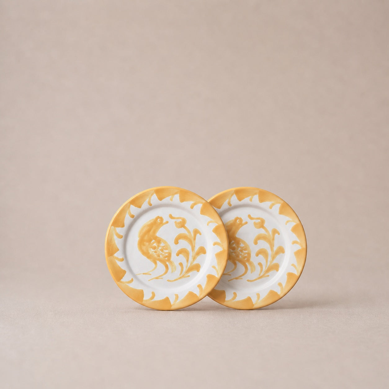 Two ceramic plates with gold and white floral designs on a beige background