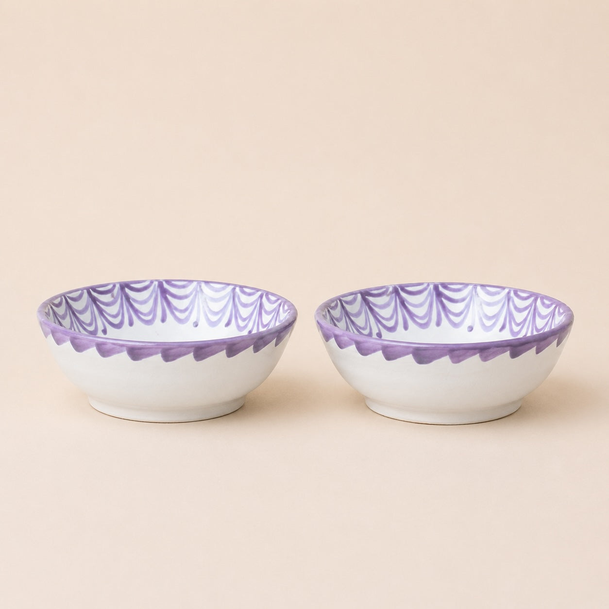 Two ceramic bowls with purple interior and rim on a beige background