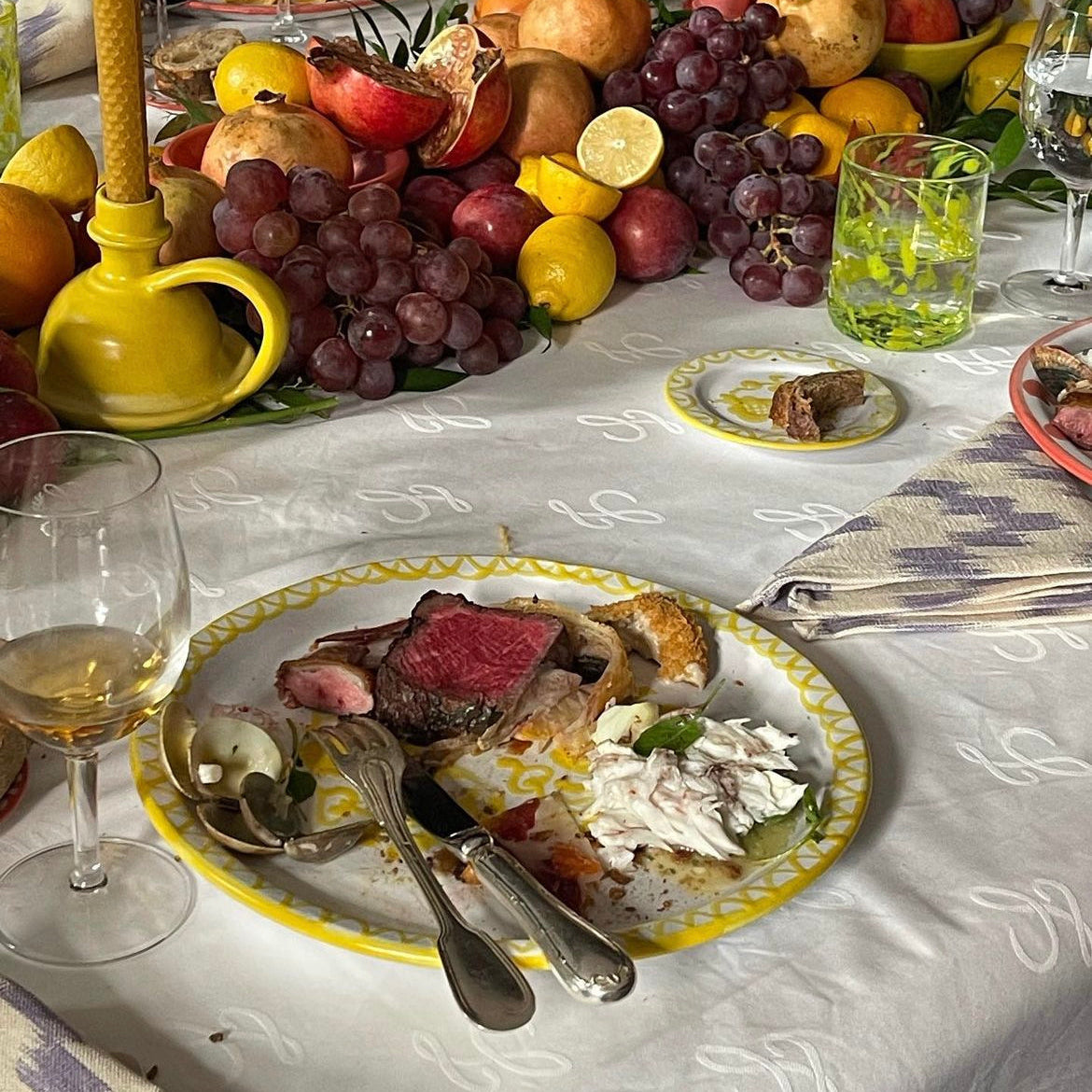 Dinner table set with a plate of food, fruits, and candles on a checkered tablecloth.