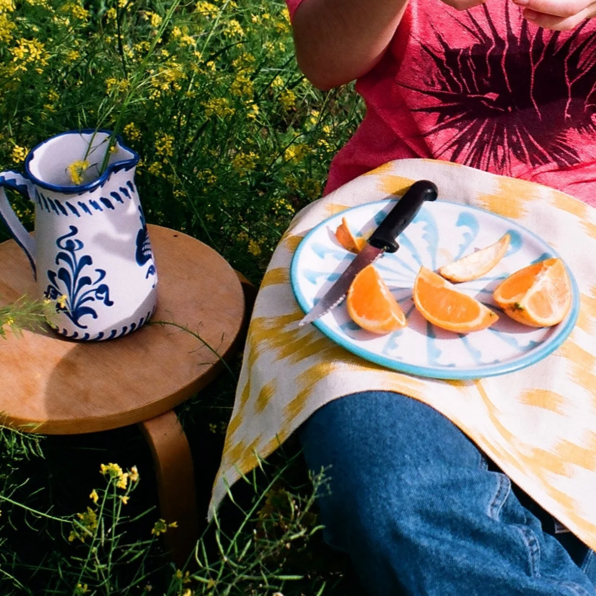 Person sitting outdoors with a plate of oranges and a ceramic pitcher on a grassy background-lifstyle
