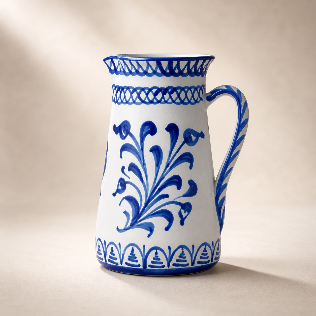 White ceramic pitcher with blue floral patterns on a beige background.