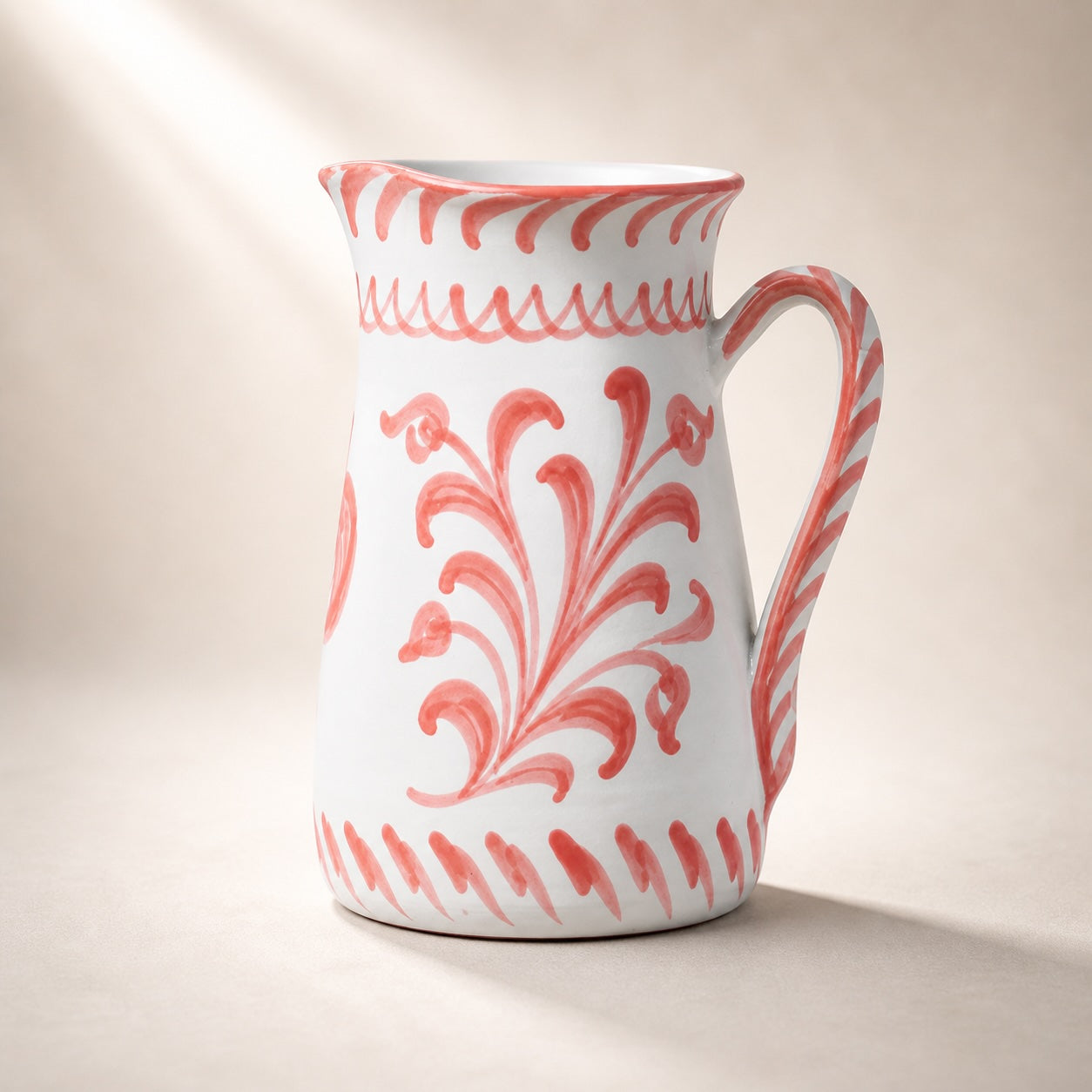 White ceramic pitcher with red floral patterns on a beige background