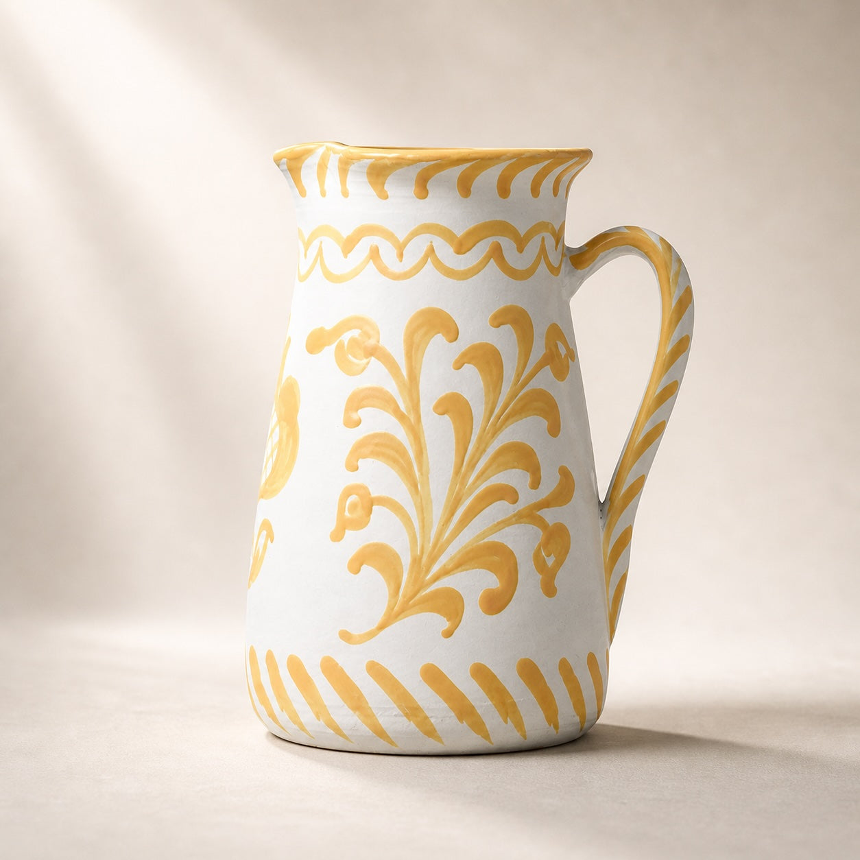 White ceramic pitcher with yellow floral patterns on a beige background