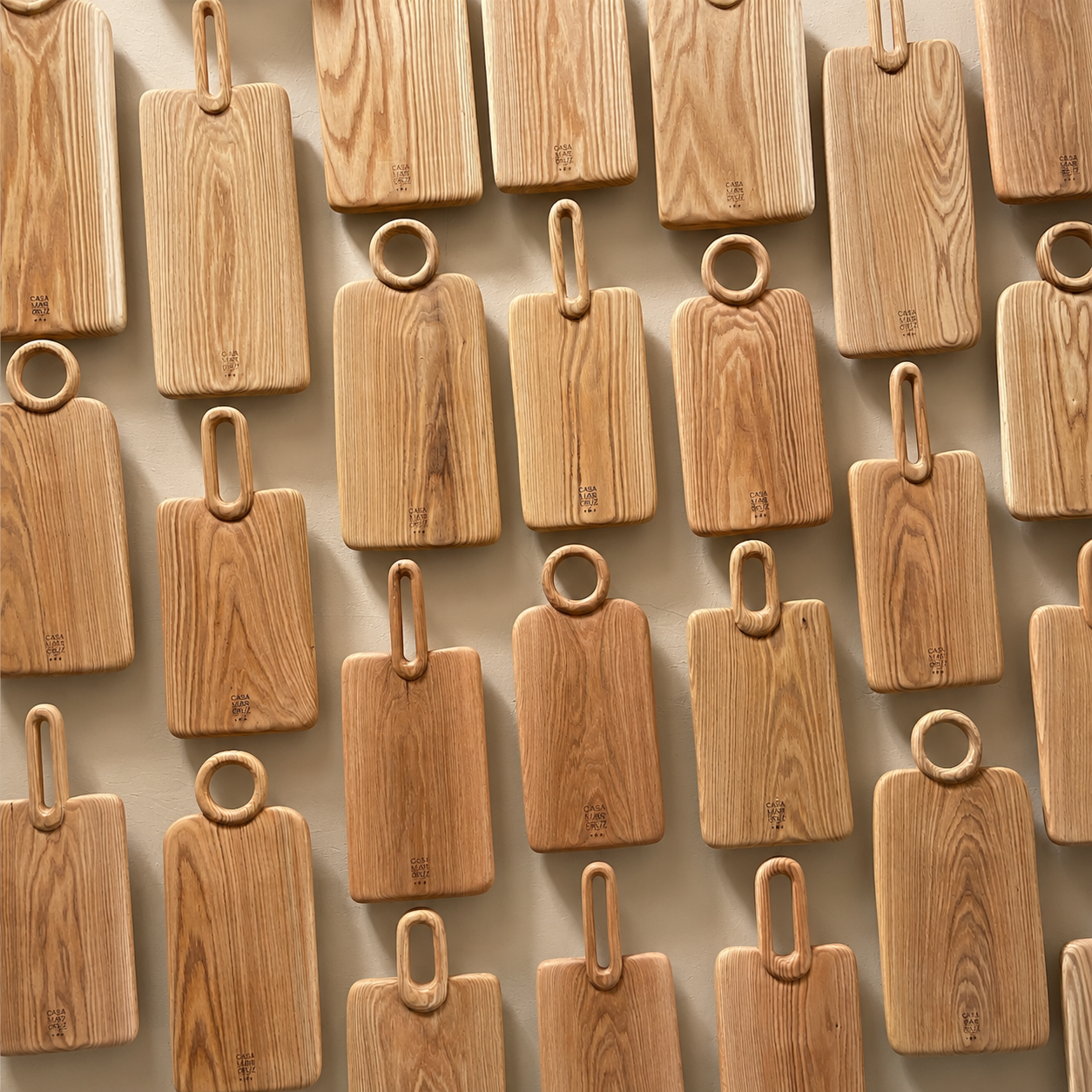 A grid arrangement of rectangular wooden serving boards with loop handles, shown from above on a light neutral background. - lifestyle